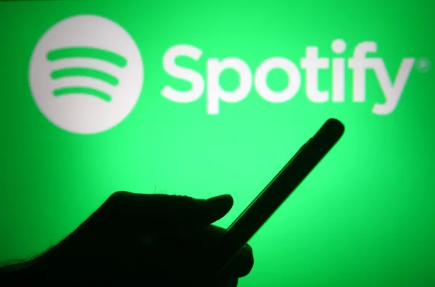 Spotify with logo in the background with a person holding a phone; Does Spotify Wrapped Include December - The Year End Musical Summary?